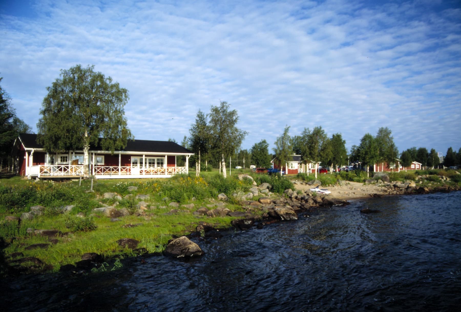 Röda stugor vid Torne älv i Kukkolaforsen i sommarljus
